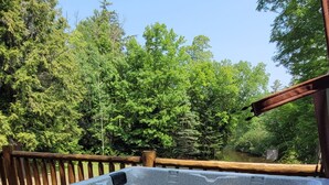 A hot tub with a wooden deck and a view of a forested area. - Seney Cabin with hot tub (Germfask)