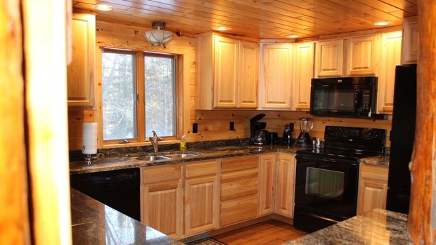A kitchen with wooden cabinets, granite countertops, a black stove, and a microwave. - Seney Cabin with hot tub (Germfask)