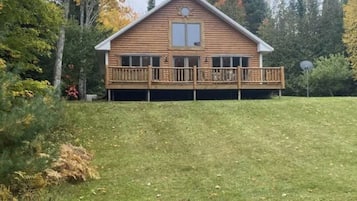 Situated on a grassy slope, this cabin features a gabled roof and a balcony.