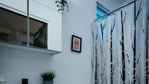 Een badkamer met een wit toilet, een wastafel met een plant, een ingelijst beeld aan de muur en een douchegordijn met een boompatroon.