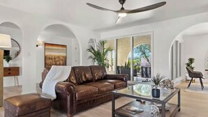 A spacious living room with a brown leather sofa, a glass coffee table, and a ceiling fan. - 6 bd Desert Oasis w/ Pool, Slide, Pickleball+More! (Scottsdale)