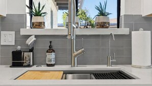 A modern kitchen with a stainless steel sink, a window with potted plants, and a view of the outdoors. - 6 bd Desert Oasis w/ Pool, Slide, Pickleball+More! (Scottsdale)