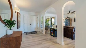 A spacious living area with a wooden floor, a large mirror, a potted plant, and a brown leather sofa. - 6 bd Desert Oasis w/ Pool, Slide, Pickleball+More! (Scottsdale)