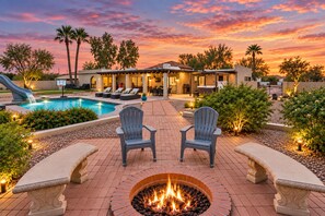 A poolside area with a fire pit, lounge chairs, and a house in the background.