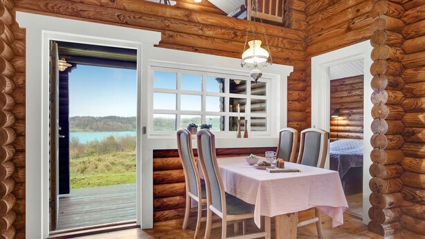 A log cabin interior with a dining table set for two, a view of a lake, and a wooden ceiling. - 2 bedroom cozy home in Mariager (Mariager)