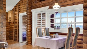 A log cabin interior with a dining table, chairs, and a window with multiple panes. - 2 bedroom cozy home in Mariager (Mariager)