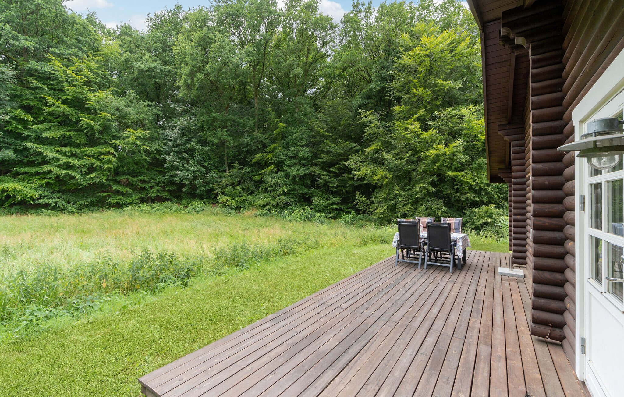 A wooden deck with two tables and chairs, surrounded by lush greenery and trees.