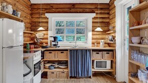 A compact kitchen with wooden walls, a window with multiple panes, and various kitchen appliances. - 2 bedroom cozy home in Mariager (Mariager)