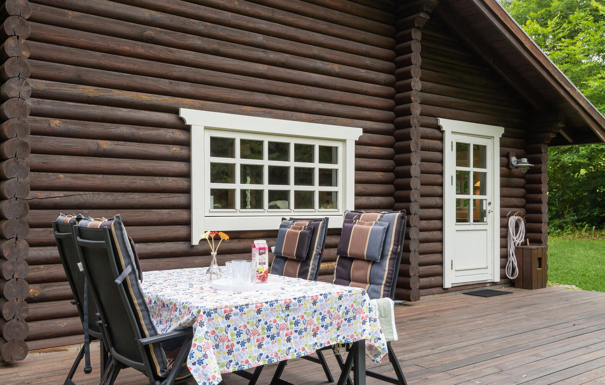 A log cabin with a deck, a table with chairs, and a window.