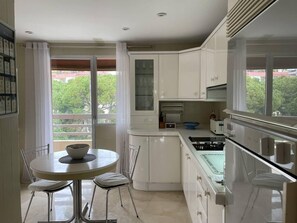 A modern kitchen with white cabinets, a round dining table, and a view of greenery outside. - Pent-House, 3 Bedroom, Sleeps 6, Parking (Marbella)