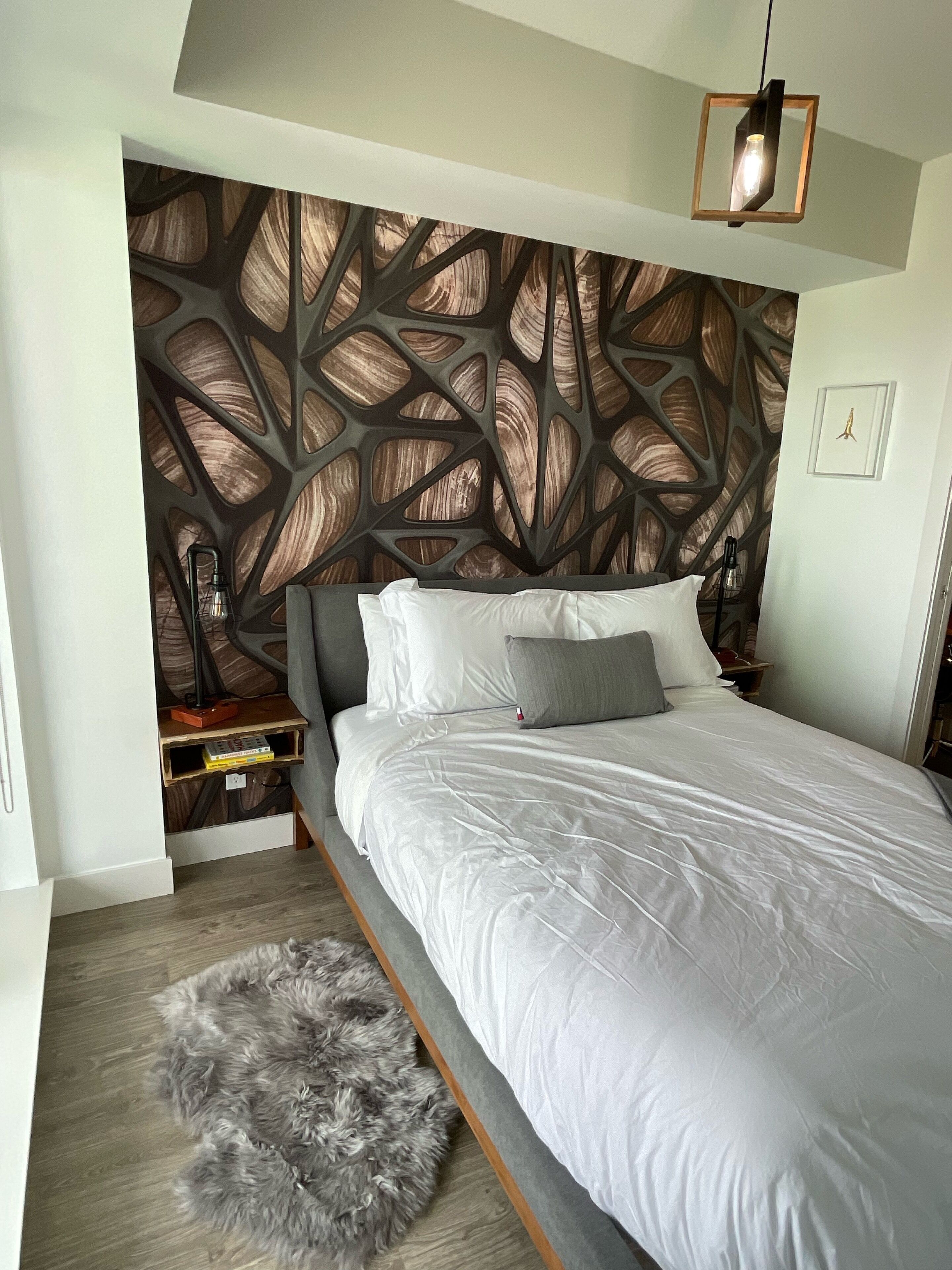 Une chambre moderne avec un grand lit, un panneau décoratif au mur, une petite table d’appoint et un tapis moelleux.