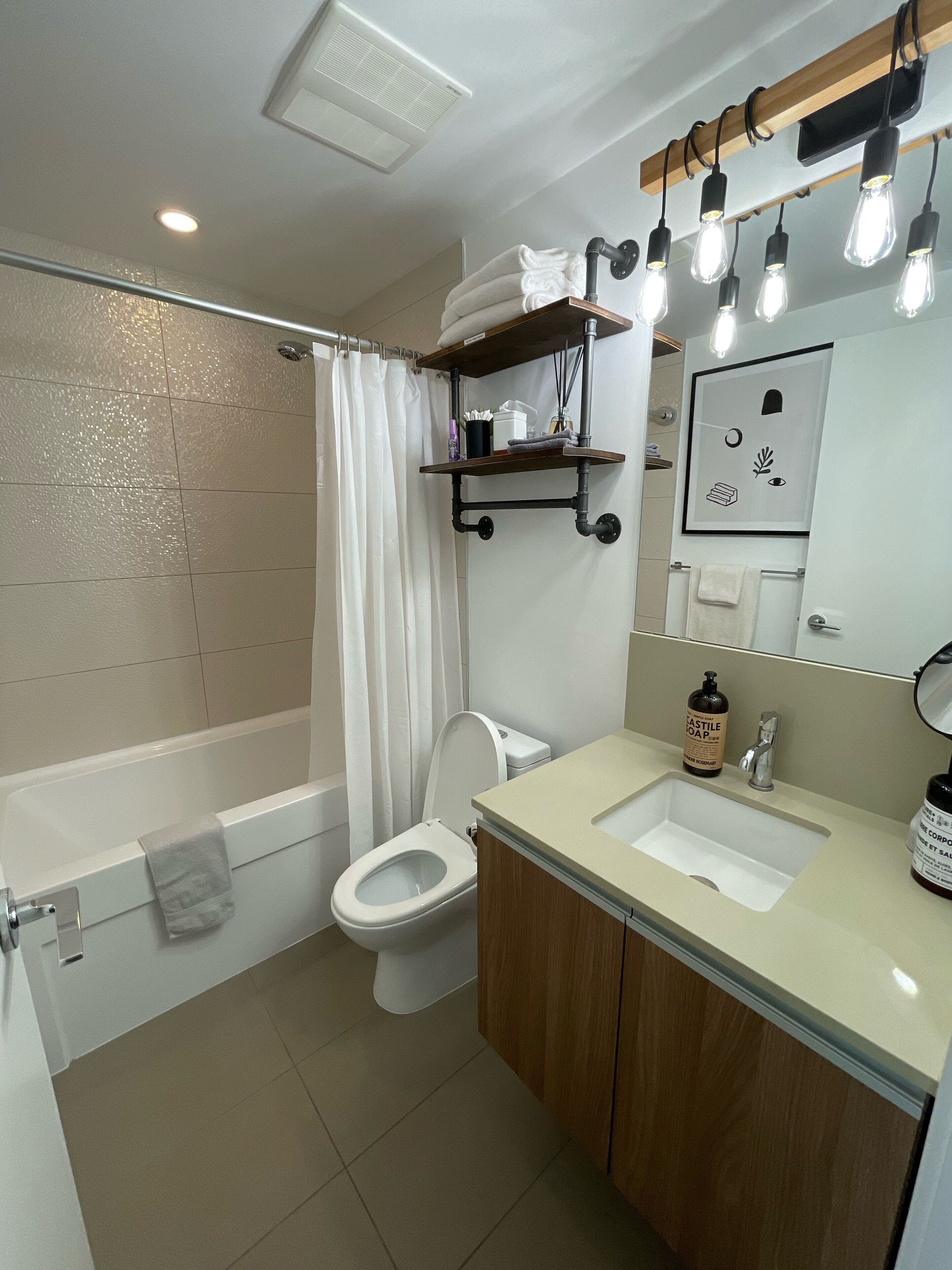 Un baño moderno con bañera, inodoro y lavamanos. Hay repisas sobre el lavamanos y una cortina de ducha.