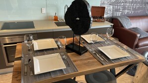 Un comedor con una mesa de madera dispuesta para cuatro, una cocina moderna al fondo y un sofá de cuero.