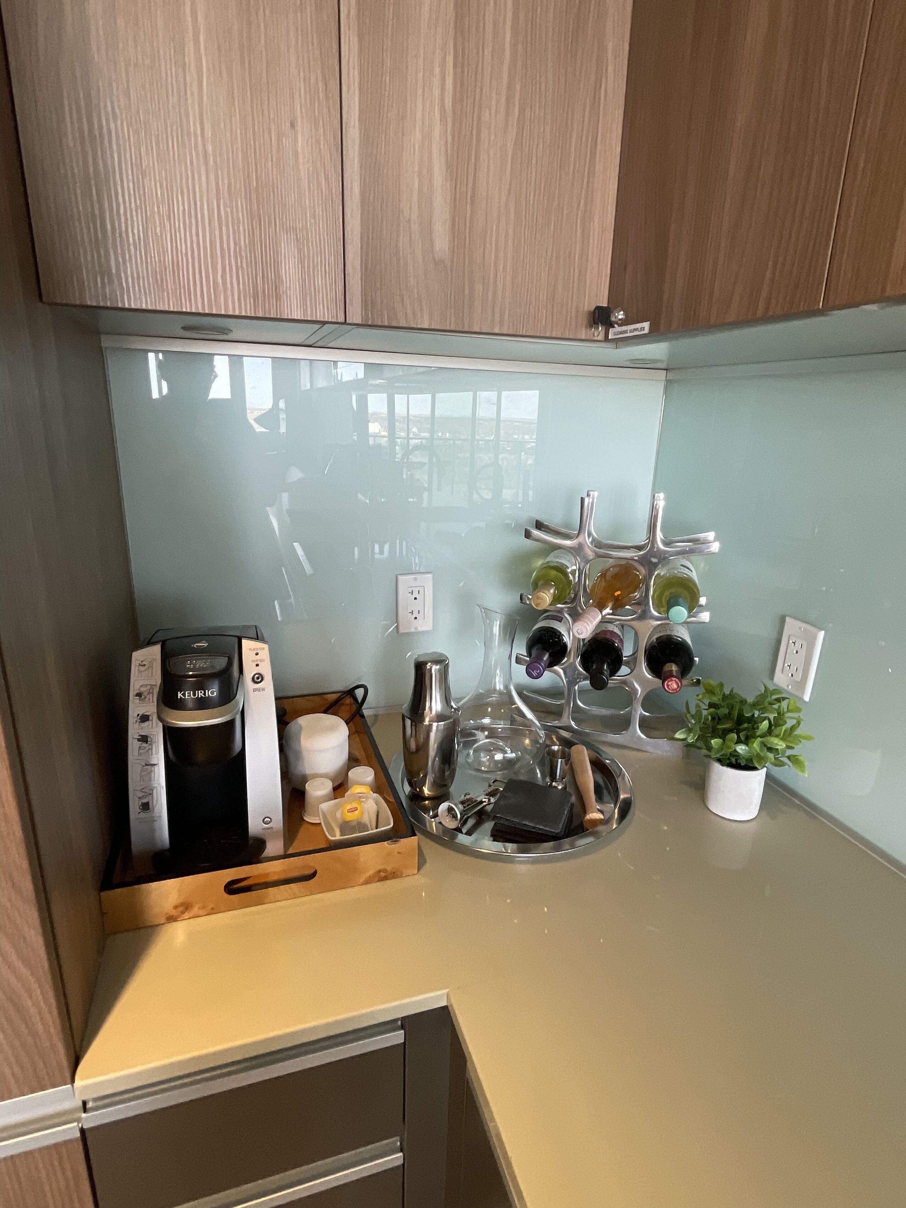 Une cuisine avec des meubles de rangement en bois, une machine à café, un porte-bouteilles et une petite plante en pot.