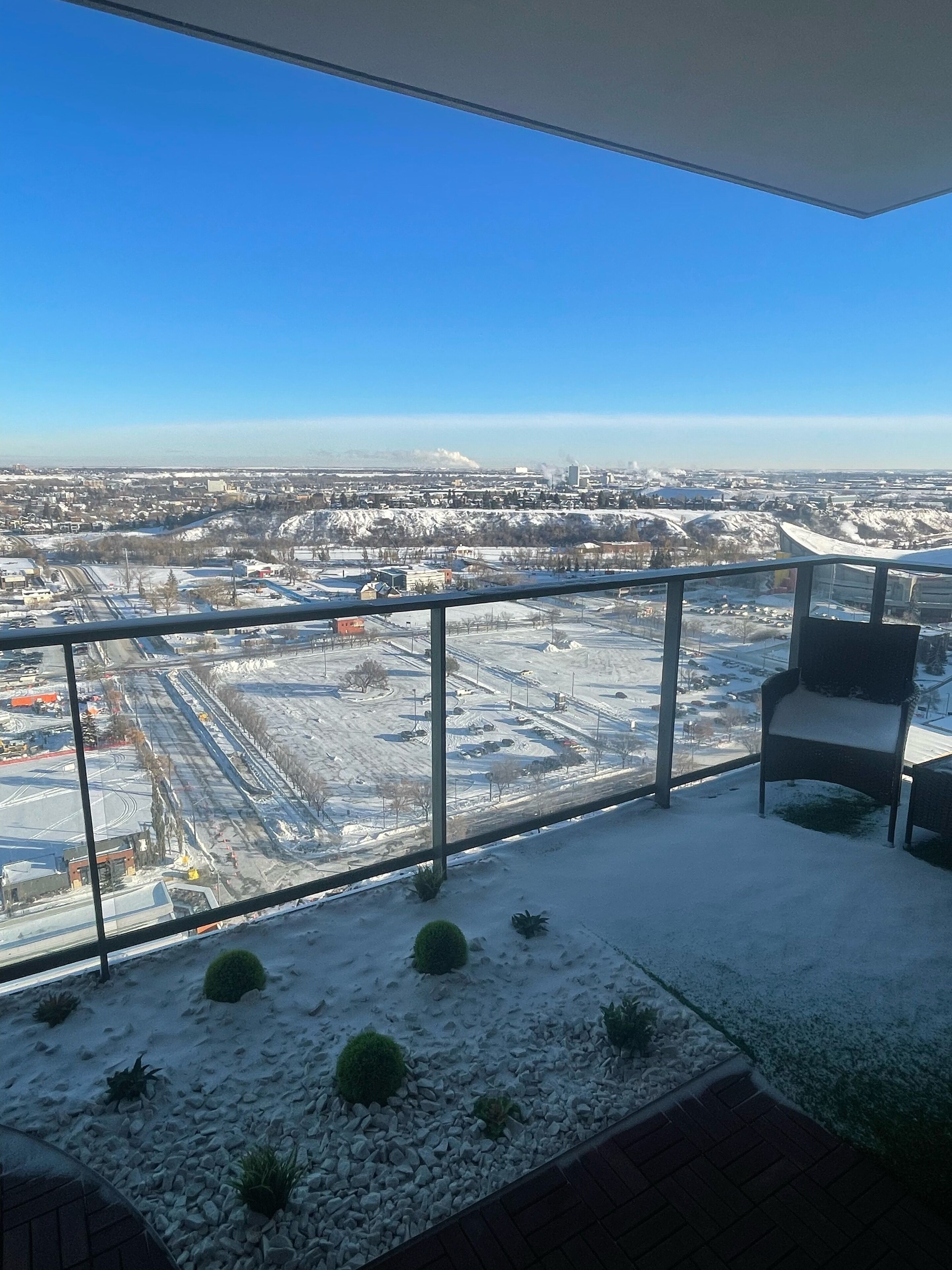 Een balkon met een helder uitzicht op een besneeuwd landschap en verre gebouwen.