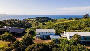 A modern house with a large deck, surrounded by lush greenery and a view of the ocean. - Palm Ridge - near Onetangi & Palm Beach (Waiheke Island)