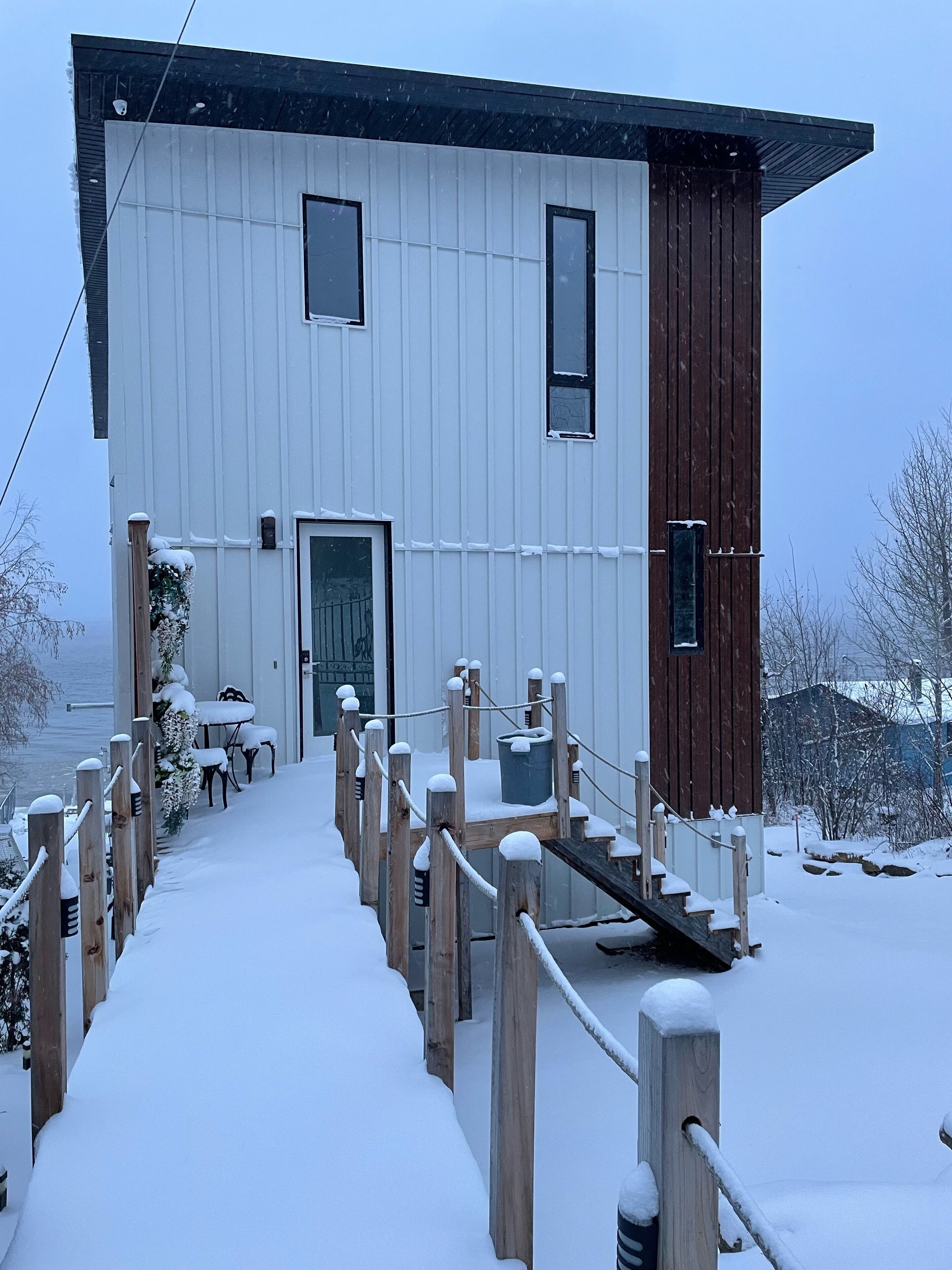 Un bâtiment blanc avec une partie en bois, un escalier menant à une porte et un chemin recouvert de neige.