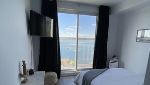Ein Schlafzimmer mit einem großen Bett, einem Schreibtisch, einem Flachbildfernseher und Meerblick durch eine Schiebetür.