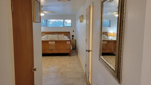 A narrow hallway leading to a bedroom with a wooden bed, a large mirror, and a window with blinds. - Comfortable Spacious Newly Renovated 3br-2ba House (Tucson)