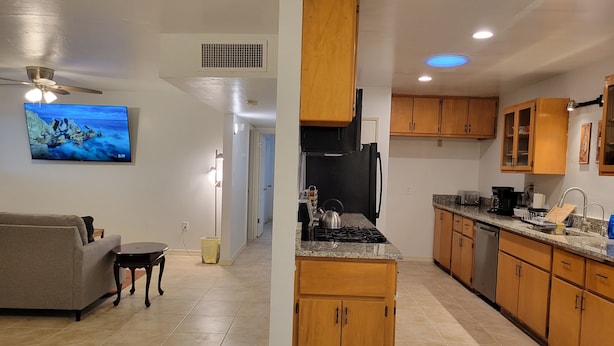 A modern kitchen with wooden cabinets, a gas stove, and a built-in oven. There is a dining area with a gray sofa and a small table. - Comfortable Spacious Newly Renovated 3br-2ba House (Tucson)