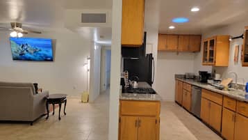 A modern kitchen with wooden cabinets, a gas stove, and a built-in oven. There is a dining area with a gray sofa and a small table.