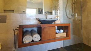 Een moderne badkamer met een douchecabine van glas, een grote spiegel en een houten wastafelmeubel met handdoeken.