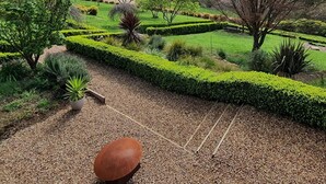 Een tuin met strakke hagen, diverse bomen en een zitgedeelte met een bank en een grote plantenbak.