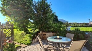 Une terrasse avec une table ronde et des chaises, entourée de verdure et offrant une vue sur une clôture située au loin.