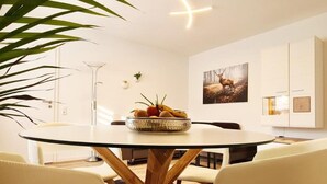 Un coin repas avec une table ronde, des chaises blanches, un saladier de fruits et un tableau accroché au mur.