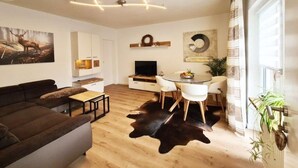 Un salon moderne comprenant un canapé, une table à manger avec des chaises, un téléviseur et un porte-manteau.