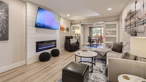 Een moderne woonkamer met een flatscreen televisie, een open haard, een bank, een salontafel en een eetgedeelte zichtbaar door een open deur.
