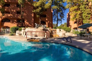 A swimming pool with a natural rock feature, surrounded by a fence and trees. - Resort Like Condo in the Prestigious Paradise Valley Area (Phoenix)
