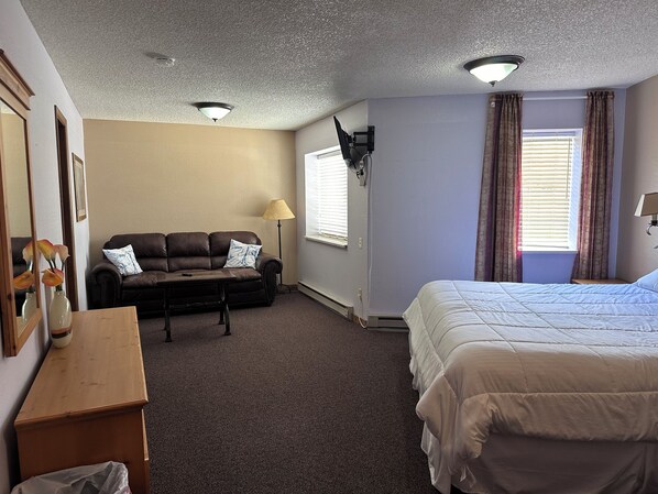 A hotel room with a bed, a sofa, a small table, a lamp, and a window with curtains.