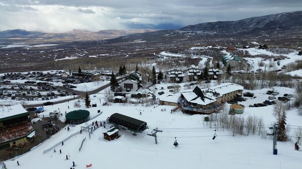 A ski resort with a ski lift, snow-covered buildings, and a parking area.
