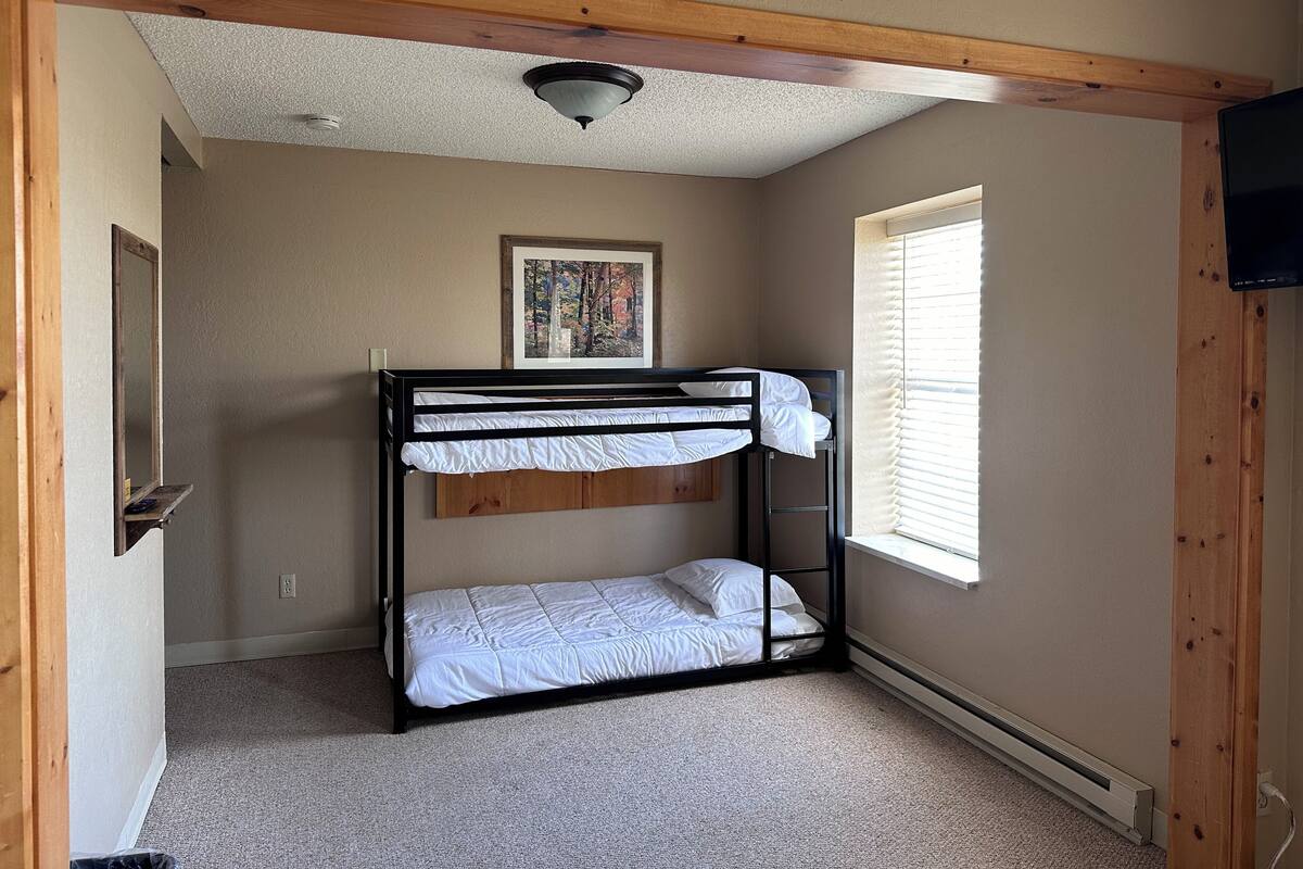 A bunk bed room with a ceiling fan, a framed picture on the wall, and a window with blinds.