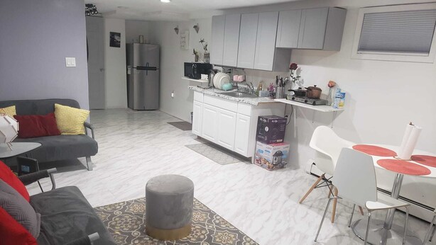 Una sala moderna con un sofá gris, un tapete estampado y un comedor con una mesa blanca y individuales rojos.