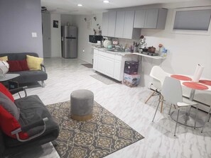 A modern living room with a grey sofa, a patterned rug, and a dining area with a white table and red placemats.