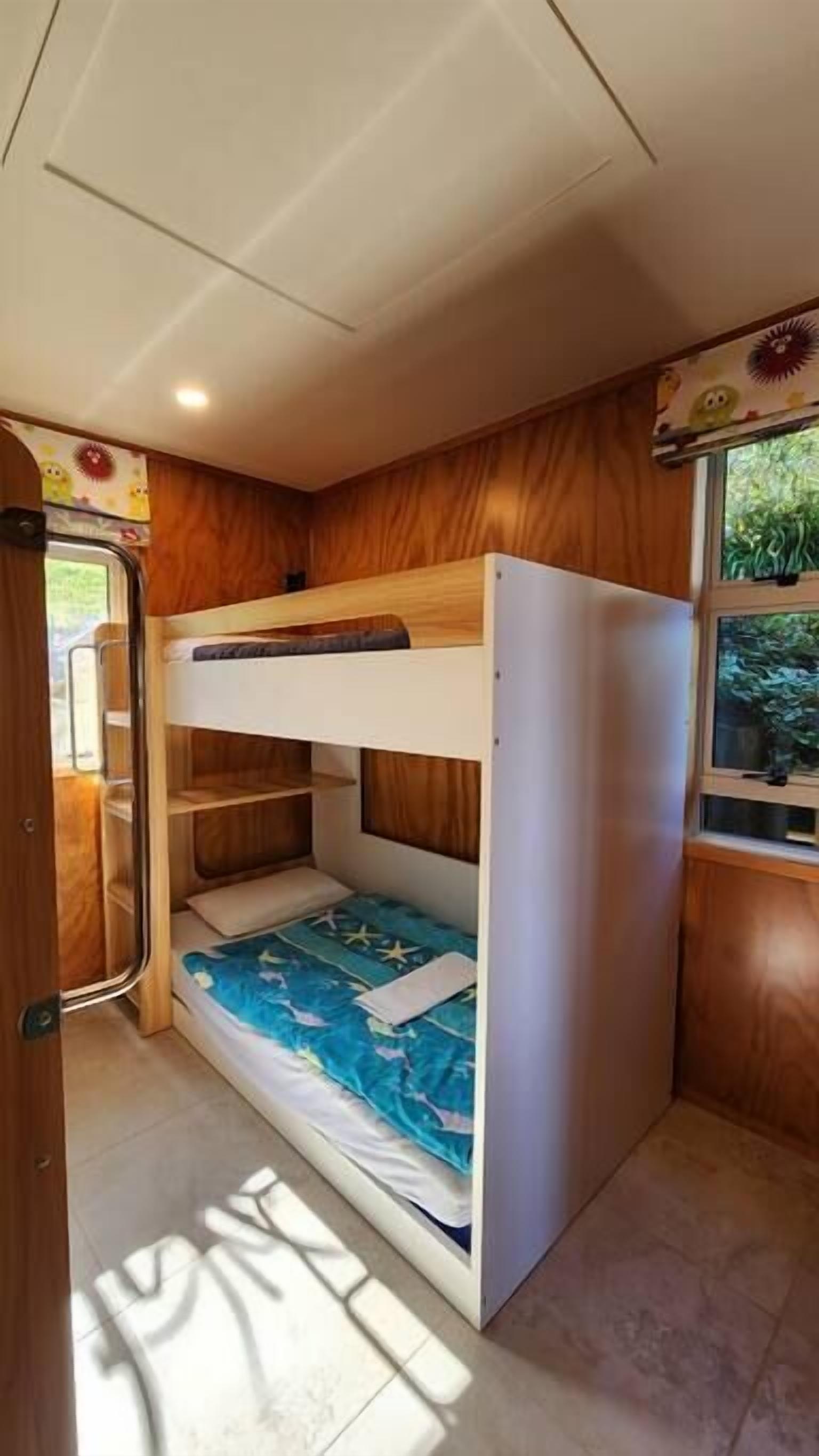 A bunk bed with a lower shelf and a window on the right.