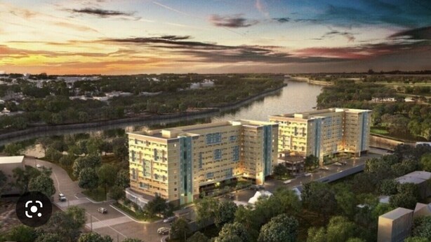Un complexe hôtelier moderne composé de plusieurs bâtiments, avec un parking et une rivière en arrière-plan.
