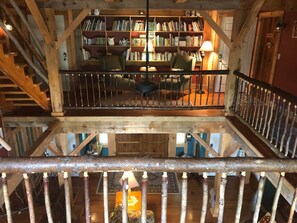 A wooden staircase leading to a balcony with bookshelves, a chair, and a table. - Yellow Barn Estate (Freeville)