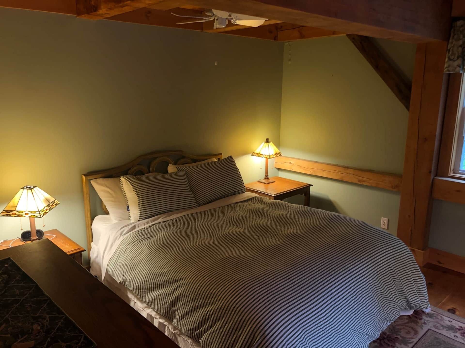 A bedroom with a bed, two bedside lamps, a wooden headboard, and a window.