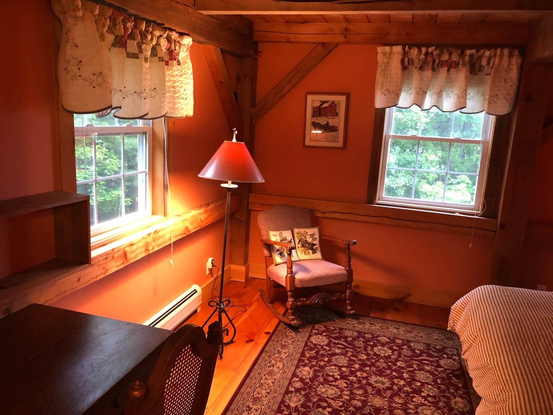 Une pièce chaleureuse avec un plancher en bois, une chaise, un bureau et une fenêtre avec des rideaux.