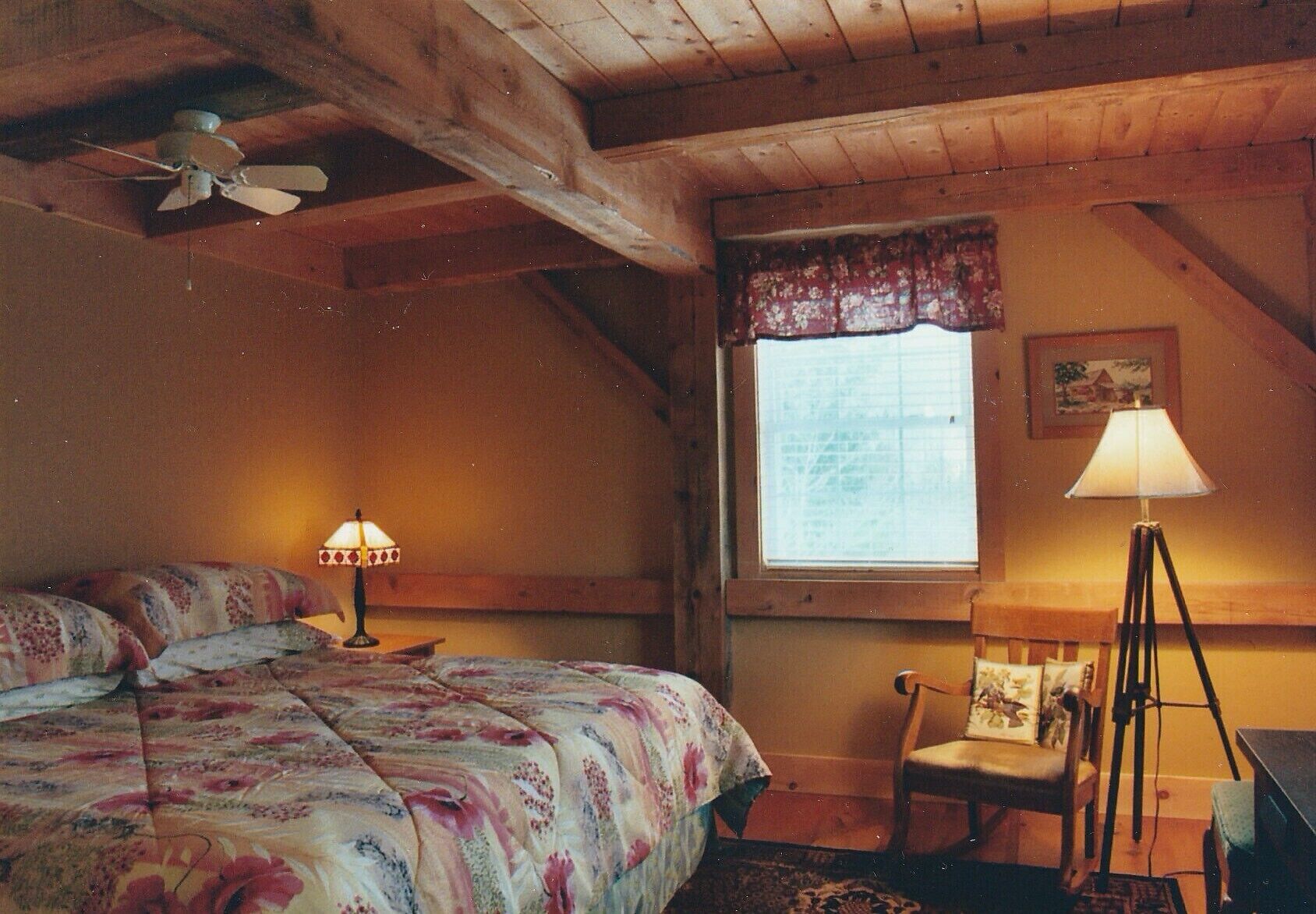 A bedroom with a bed, a desk, a chair, a lamp, a window, and a ceiling fan.