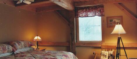 A bedroom with a bed, a desk, a chair, a lamp, a window, and a ceiling fan.