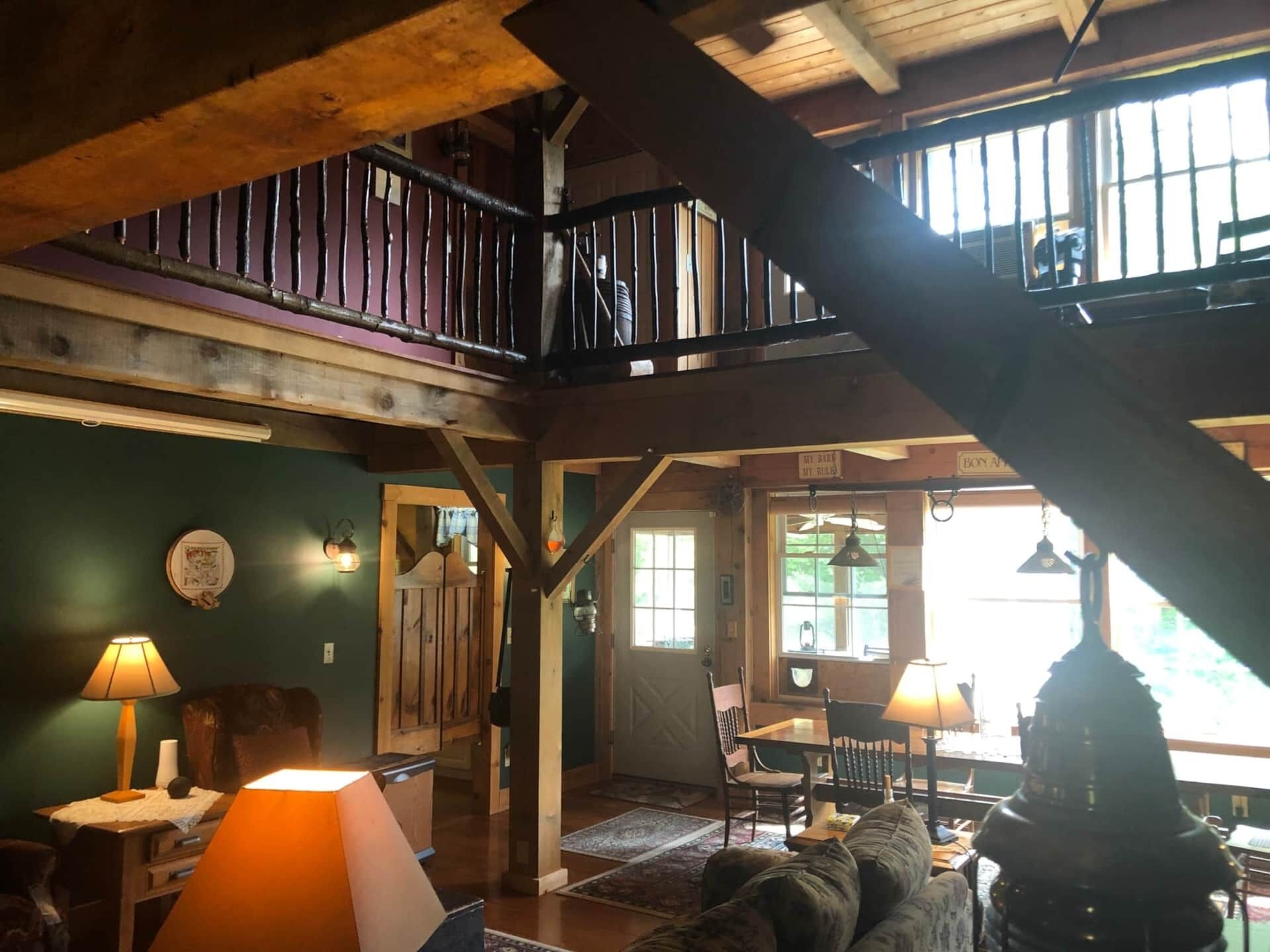 Ein geräumiger Raum mit hohen Decken, Holzbalken, einem Balkon, einem Essbereich mit Stühlen und Tisch sowie einer gemütlichen Sitzecke mit Sofa und Lampen.