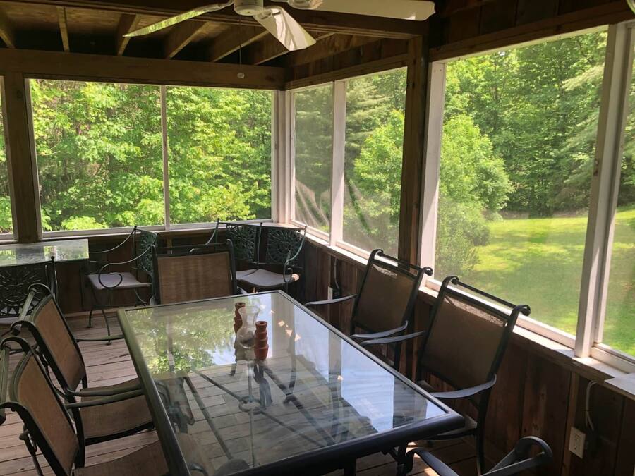 A covered patio with a glass table and chairs, large windows, and a view of a green landscape.