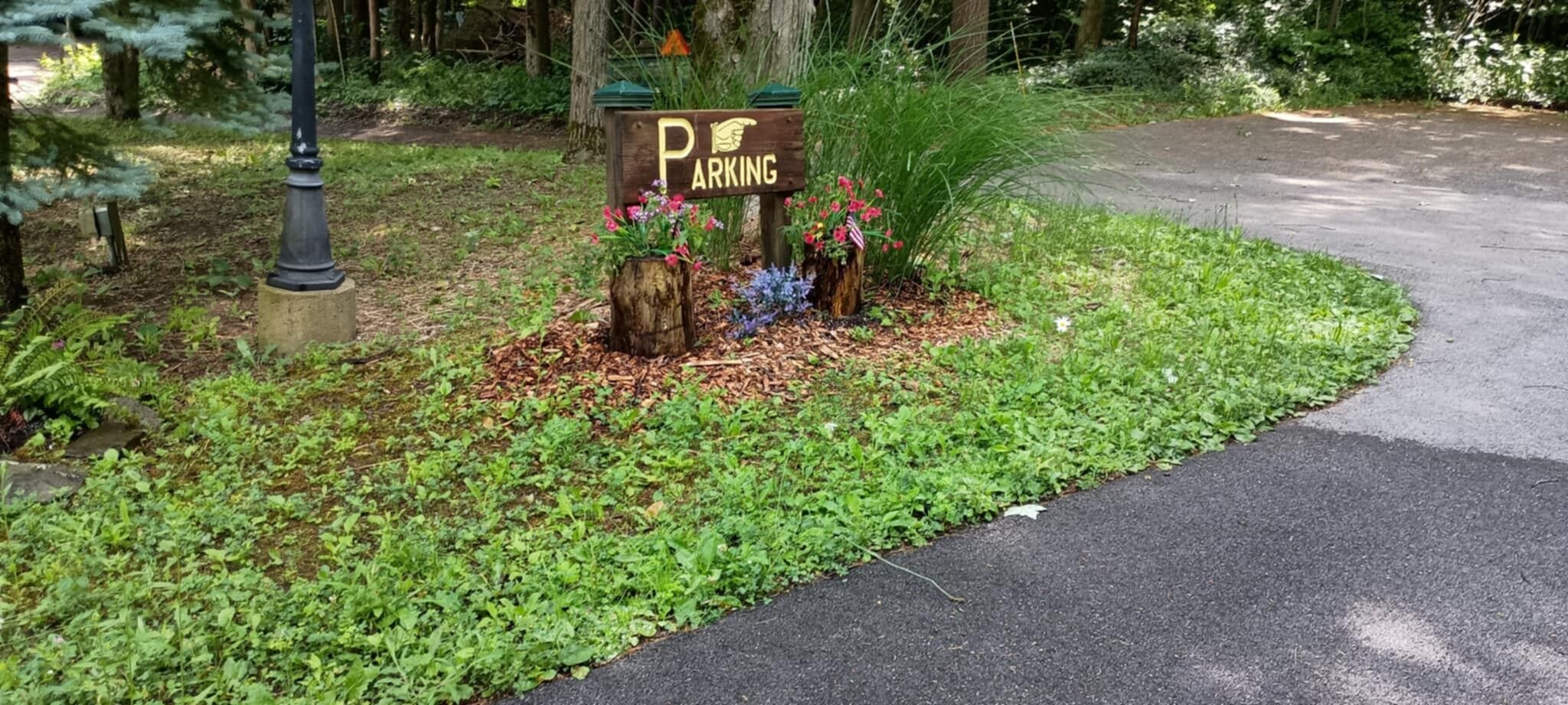 Un panneau en bois sur lequel est écrit « PARKING », entouré de verdure et de fleurs.