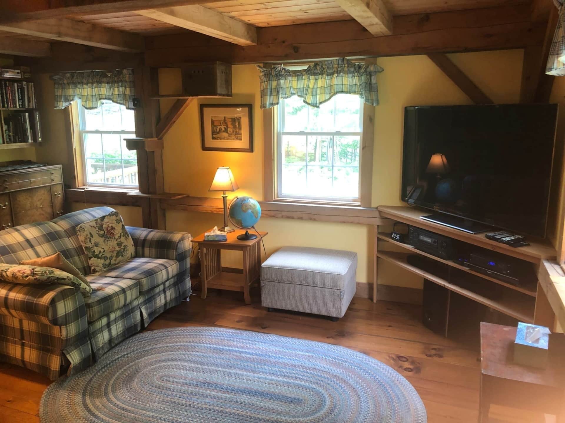 Un salon chaleureux avec un canapé à carreaux, une petite table d’appoint avec une lampe et un globe terrestre, un téléviseur et un meuble de rangement en bois.