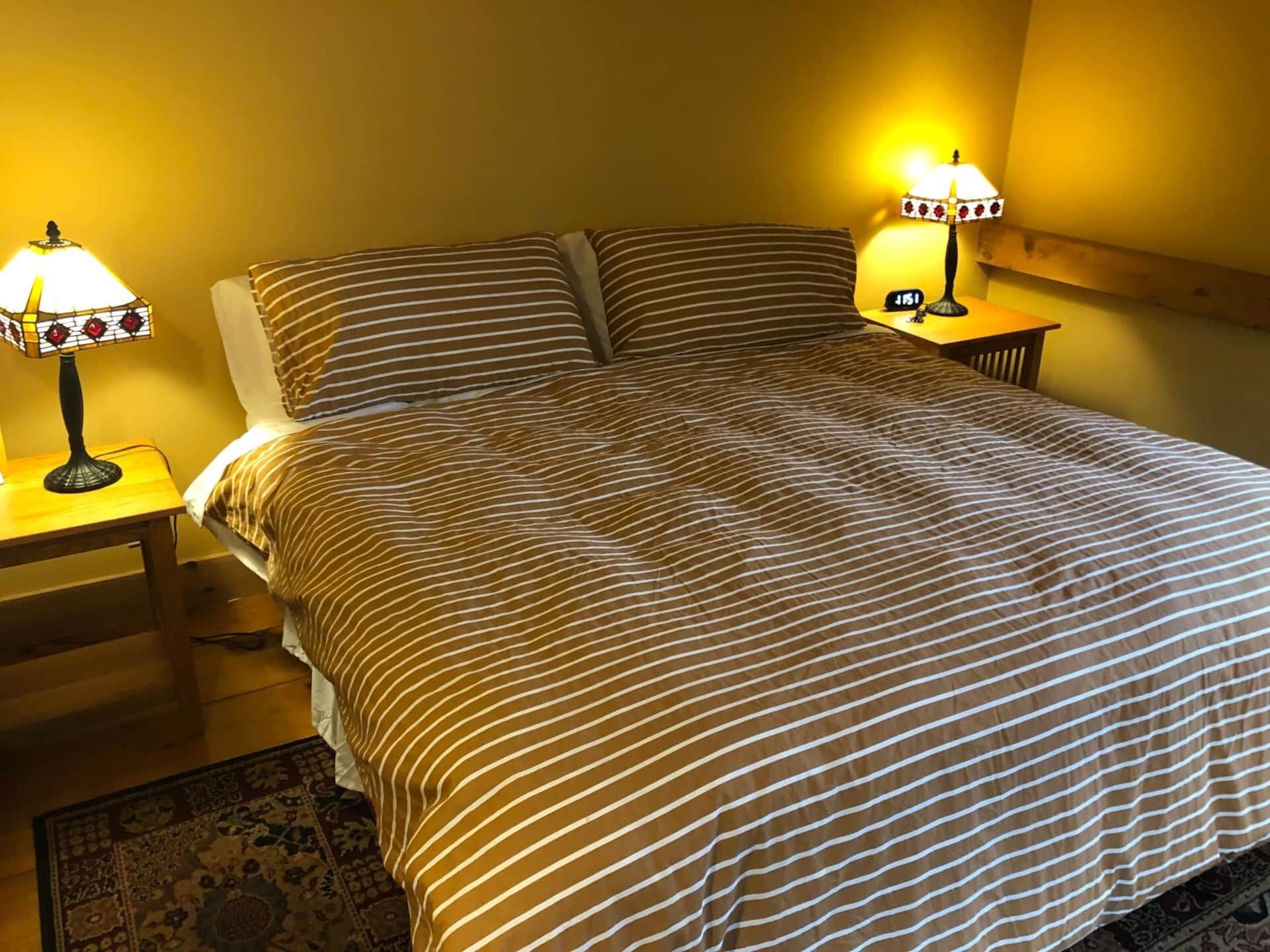 A neatly made bed with striped bedding, two bedside lamps, and a wooden nightstand.