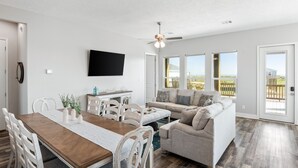 A spacious living room with a dining area, a sofa, and a TV mounted on the wall. - Beach View Retreat w/ Huge Covered Patio + Games (Bolivar Peninsula)